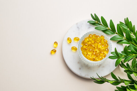 Yellow softgel vitamins capsules in a bowl on a marble stand on a light background