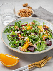A fresh salad of beets, orange, and arugula with feta, walnuts, and balsamic dressing on a plate