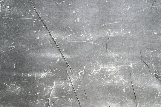 Texture of a gray scratched metal or plastic surface with cracks and abrasions. Industrial grunge background ideal for overlays, distressed effects, aging designs, and gritty visual compositions.
