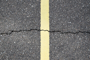 Fototapeta premium Cracked asphalt road surface with a yellow traffic line. Urban street texture background showing wear and damage, ideal for transportation concepts, road safety themes, and gritty design projects.