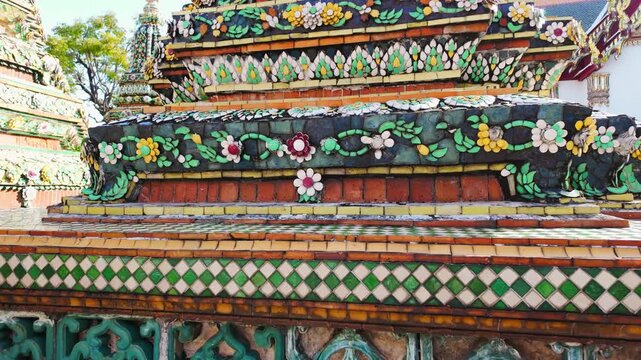Video view of ornate stupas and Wat Pho temple in Bangkok, Thailand, highlighting richly decorated towers covered with colorful ceramic floral patterns in bright daylight.