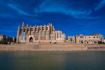 Waterfront cityscape with historic buildings, palm trees and a modern sculpture rising from the water under a clear blue sky