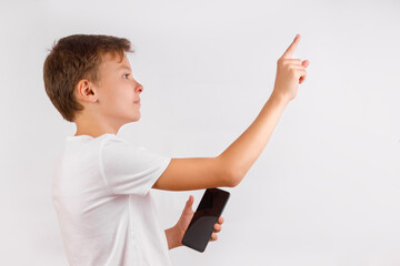 Side profile of a young boy in a white T-shirt, holding a black smartphone in his right hand and extending his left arm to point upwards