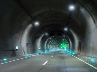 Modern illuminated road tunnel with curve green light and ventilation system.