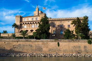 Historic fortress and palace beside the waterfront under a blue sky. Mediterranean landmark with stone walls, palm trees and reflections.
