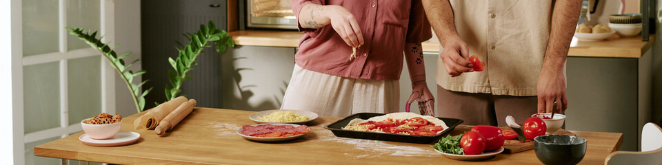 Website banner of woman and man preparing homemade pizza together in kitchen, arranging toppings on dough with various ingredients on wooden table