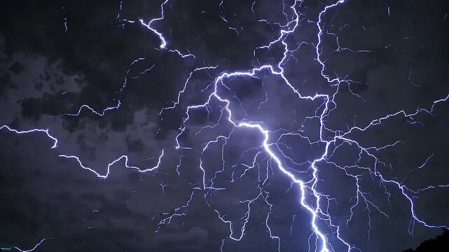 During a fierce thunderstorm, the sky is lit up by a dazzling display of electrical energy. Vibrant blue and purple lightning bolts streak across the ominous, cloud filled night sky