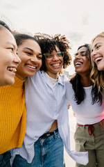 Smiling women hugging outdoors in a warm friendly moment. A diverse group expressing affection and spontaneous joy together. Togetherness and wellbeing concept.