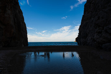 Mediterranean coastal landscape with calm sea, natural reflections and rocky cliffs framing the blue horizon.