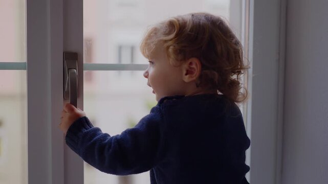 Toddler reaching for window handle and attempting to open it without success while standing indoors near glass frame highlighting child safety concerns around accessible home window