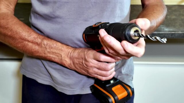 Mature handyman's hands inserting a metal bit into the chuck of a black and orange power drill, getting ready to work on a do-it-yourself project in his home workshop or garage