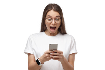 Fototapeta premium Close-up portrait of young female in white t-shirt, holding phone, looking surprised and shocked