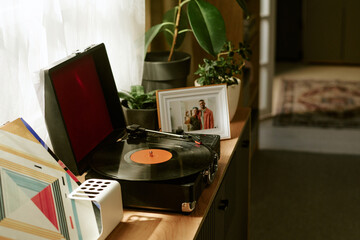 Vinyl record player spinning on wooden cabinet near potted plants and framed photo of smiling man and Caucasian woman standing together