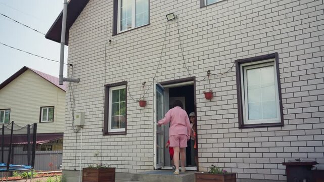 Mother Helps Child, Lady In Pink Supports Child Navigating Garden Steps And Play Zone, Woman Dressed In Pastel Guides Young Child Across Garden Steps Into Cozy House Amid Playful Surroundings