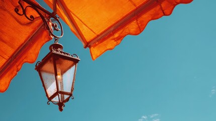 Low-angle view of an illuminated antique lantern suspended under an orange awning against a vibrant, cloudless azure sky