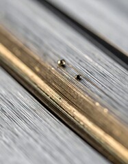 Macro shot of two minuscule metallic spheres resting on a finely grooved surface next to a polished golden bar.