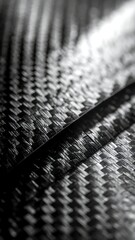 Close-up view of a dark woven carbon fiber texture with a diagonal seam, highlighting its intricate pattern and material strength.