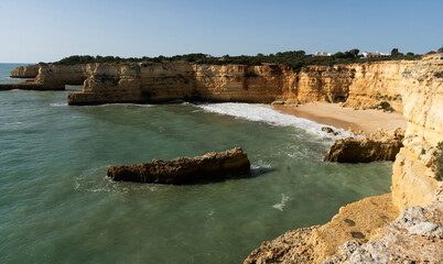 Beautiful sandy beach with red rocks and cliffs. Sunset at dusk with shallow waves on the Atlantic coast in Praia do Barranco, Praia do Pontal, Algarve, Portugal