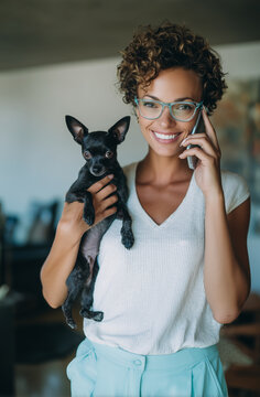 Escena dom&eacute;stica que evoca la multitarea afectuosa, el v&iacute;nculo con las mascotas y el bienestar cotidiano en un ambiente acogedor. Una persona con gafas sostiene a un perro peque&ntilde;o mientras habla 
