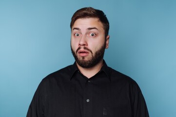 Man shows surprise with wide eyes and open mouth in front of plain blue background during casual moment