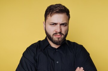 Man with beard shows serious expression against yellow background in indoor setting