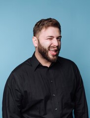 Obraz premium Man smiles and winks against a blue backdrop while wearing a black shirt and showing a playful expression