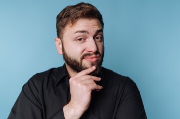 Obraz premium Man with beard thinking in front of a light blue background during a casual moment