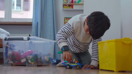 Child playing with toy vehicle on floor near storage bins, focused imagination and absorbed attention during quiet indoor playtime at home