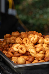 Bulk supply of classic mini donuts, bite-sized traditional donuts in a metal tray. The small one-bite golden cake donuts are a deep-fried snack. The dense, moist cake bites are warm and crusty.