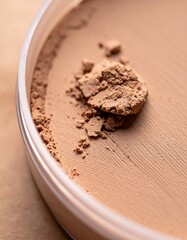 Close-up of beige loose face powder in a clear container, showing its fine texture and scattered particles.