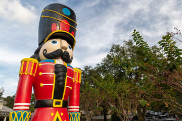 A large nutcracker soldier decoration standing outdoors with trees and a cloudy sky in the background. The colorful drummer ornament is made from plastic and is painted red, black, yellow, and green. 