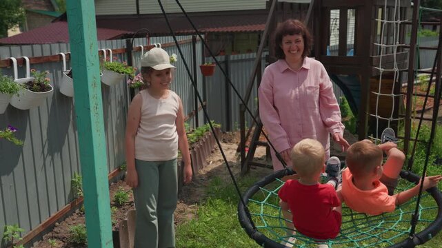Woman And Girl Watching Children In Garden, Caucasian Woman And Young Girl Supervising Young Children Outside, Lightskinned Woman And Her Daughter Observe Toddlers Playing In Blooming Yard