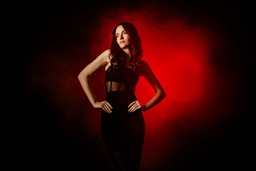 Sensual Elegant young woman in black dress posing in dramatic red illumination with stylish presence