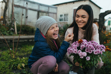 A child, a teenage girl in a garden, a vegetable garden, laughing, having fun with her mother, a young woman, with a bouquet of chrysanthemum flowers in autumn in nature.