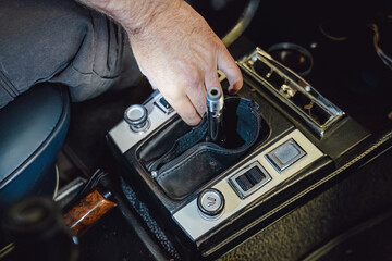Mechanic's hand installing or repairing the center console trim around the gear shift lever inside a vintage car.