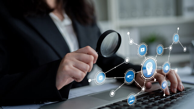 A business professional uses a magnifying glass to examine data on a laptop while surrounded by various digital network icons, symbolizing innovation and insights in the workplace. Tessel