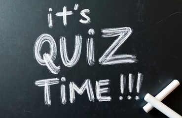 Handwritten text on chalk board says its quiz time with chalk sticks. Fun educational game sign announces competition and questions for learning.