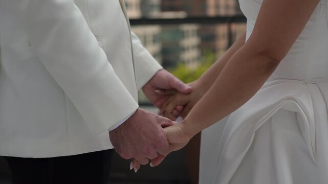 White Bride And Groom Holding Hands On Rooftop Balcony Exchanging Vows, CloseUp Of Joined Hands, White Tuxedo Jacket And Flowing Gown,