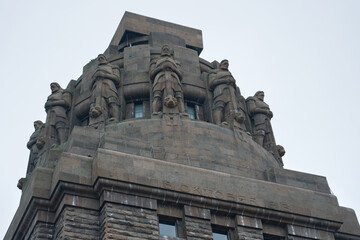 Obraz premium Monumental tower with stone figures adorning its upper section, a detailed close-up of the Völkerschlachtdenkmal's sculptural elements.