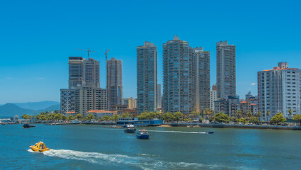 Vibrant waterfront cityscape with towering modern skyscrapers lining a clear blue bay, featuring...