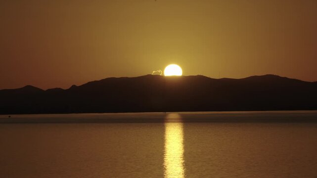Golden sun setting behind a mountain range reflecting on water
