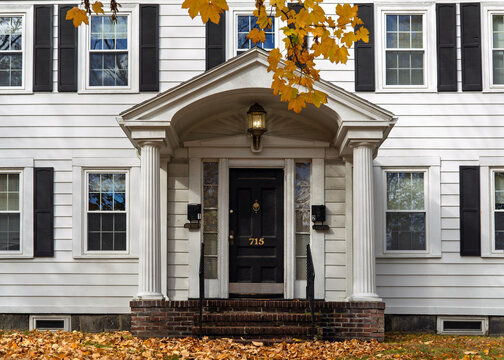 Classic New England style American family house with beautiful portico and autumn leaves in the foreground in Brighton, Boston, Massachusetts, USA
