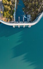 Drone photo of a dam and turquoise reservoir surrounded by forest in South Spain, ideal for...
