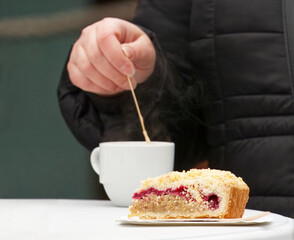 Slice of fruit cake on plate with hot coffee at Naplavka farmers market in Prague. Winter clothing and steam from the cup suggest cold advent season, relaxed moment of refreshment during market visit