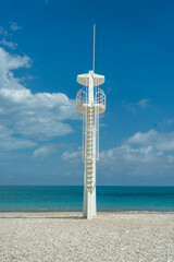 A striking white lifeguard tower stands on a tranquil pebble beach in South Spain, overlooking the...