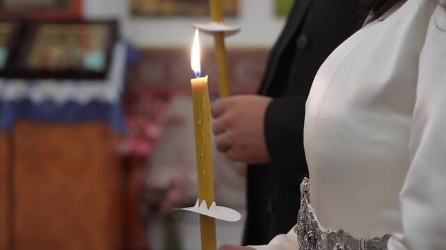 Side View Bride Holding Lit Candle Near Altar During Blessing, White Gown Sleeve And Warm Flame Create Sacred, Reflective Mood In Chapel