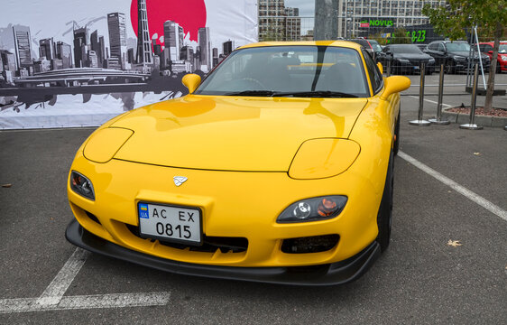 Vibrant yellow Mazda RX-7 FD sports coupe, parked outdoors at a car show. This iconic Japanese JDM car, known for its rotary engine and sleek, aerodynamic design