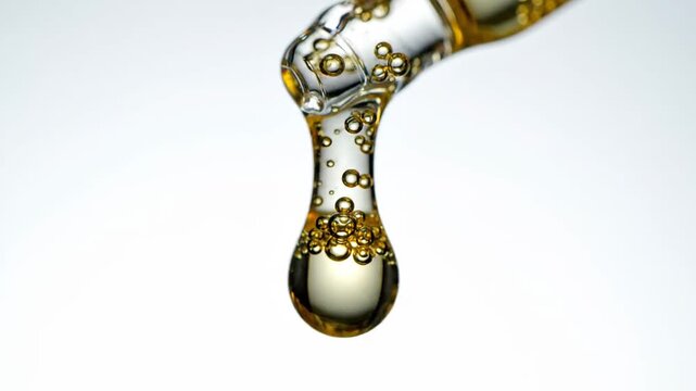 Close Up of Droplet with Bubbles Dropping from a Glass Pipette Against a Light Background