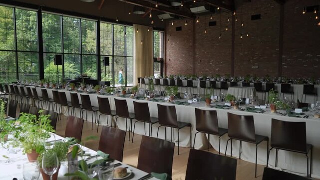 Indoor Banquet Long Table Centerpieces, Exposed Brick Wall And Tall Windows, Rows Of Chairs And White Linens, Herb And Greenery Table