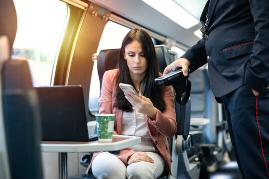 A woman pays for a train ticket using her phone. The conductor scans the train ticket with a digital payment device. Concept of digital payment and ticket reading for travel on a train.